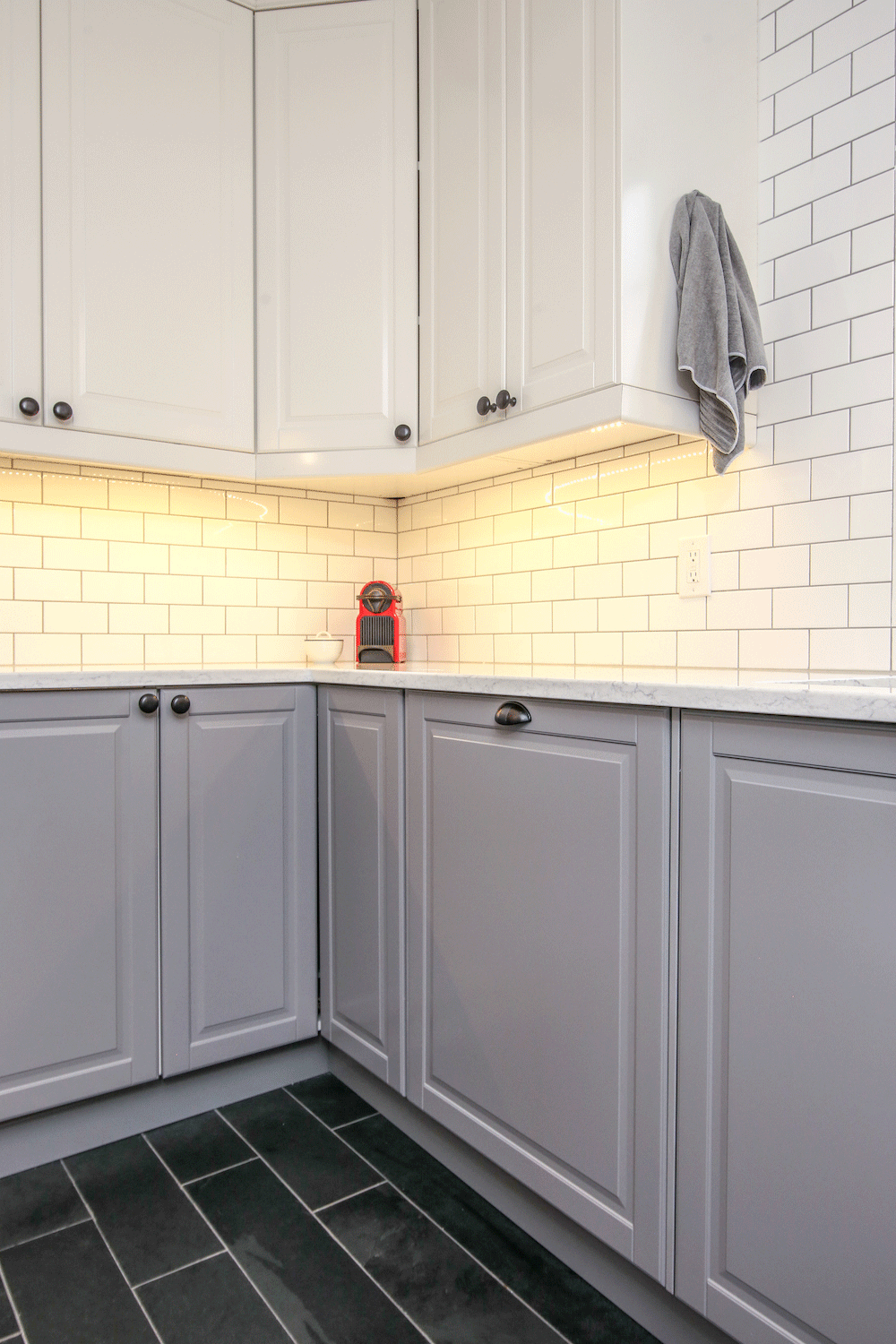 gray kitchen cabinets under white countertop and overhead kitchen cabinets with white subway tile backsplash after renovation