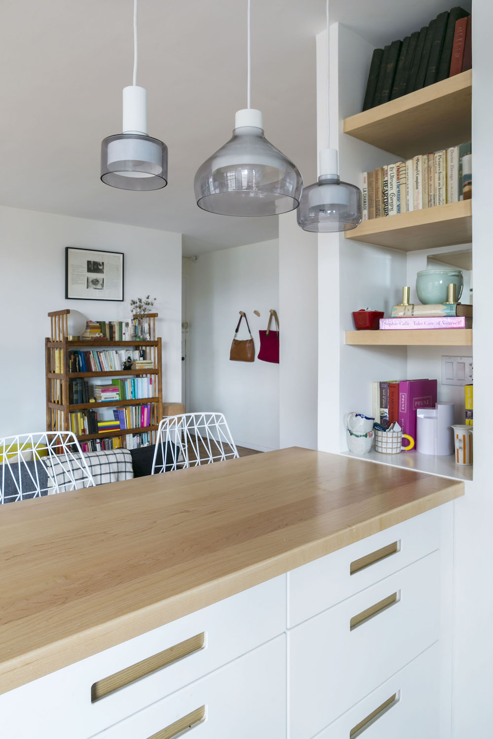 White kitchen peninsula with wooden table top and wood shelving