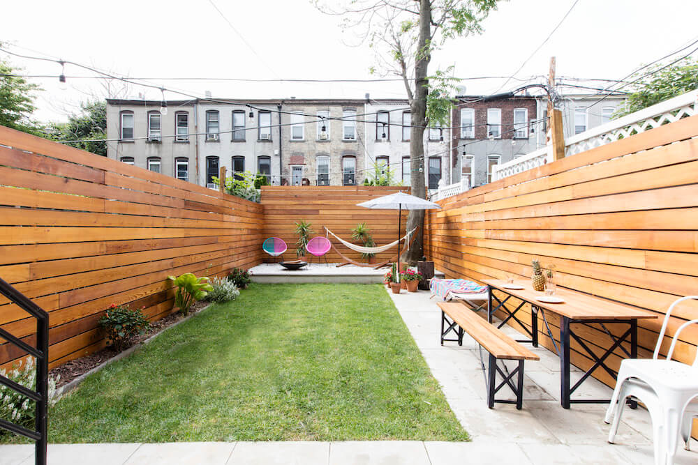 Backyard with stained cedar fencing along with white chairs and lawn grass after renovation