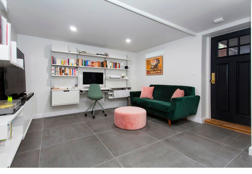 green sofa and pink poufee and cushions in an office space with white open shelves and white desk after renovation