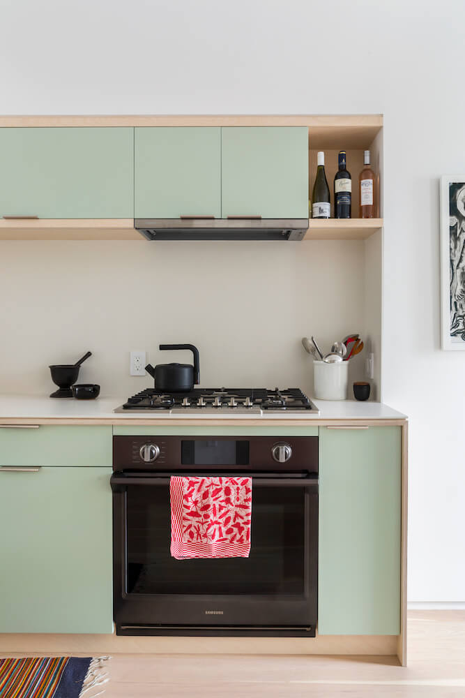 Sea green kitchen cabinets with black chimney over a black cooking range after renovation