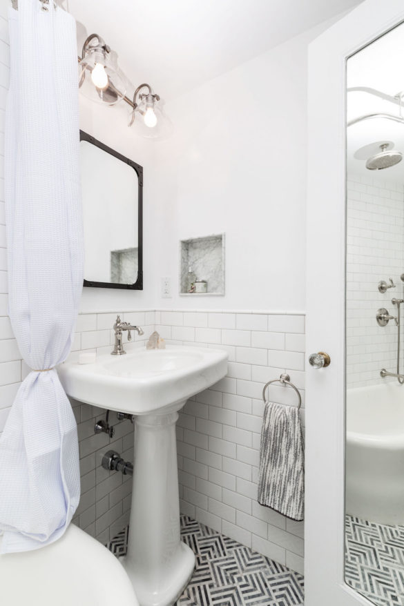 white bathroom with subway tiles and long mirror along with white pedestal sink after renovation