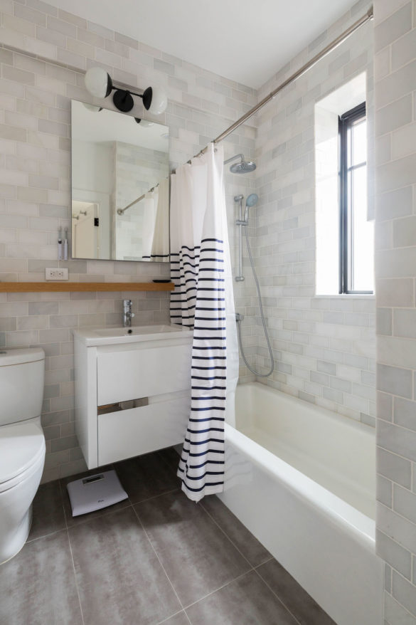 white bathroom with gray floor and white bathtub and white tiled wall after renovation