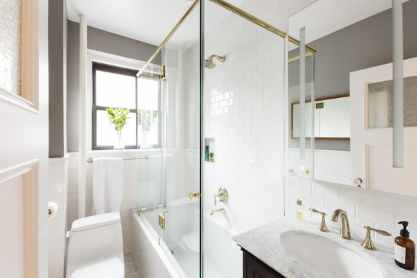 frameless glass enclosure for white bathtub in a white bathroom with white oval sink after renovation